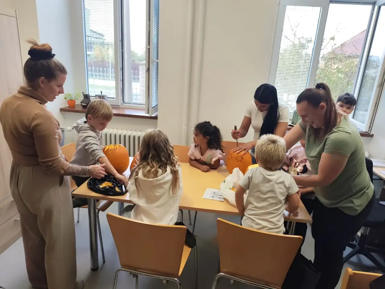 Děti a rodiče společně dlabou a vyřezávají dýně u stolu ve třídě