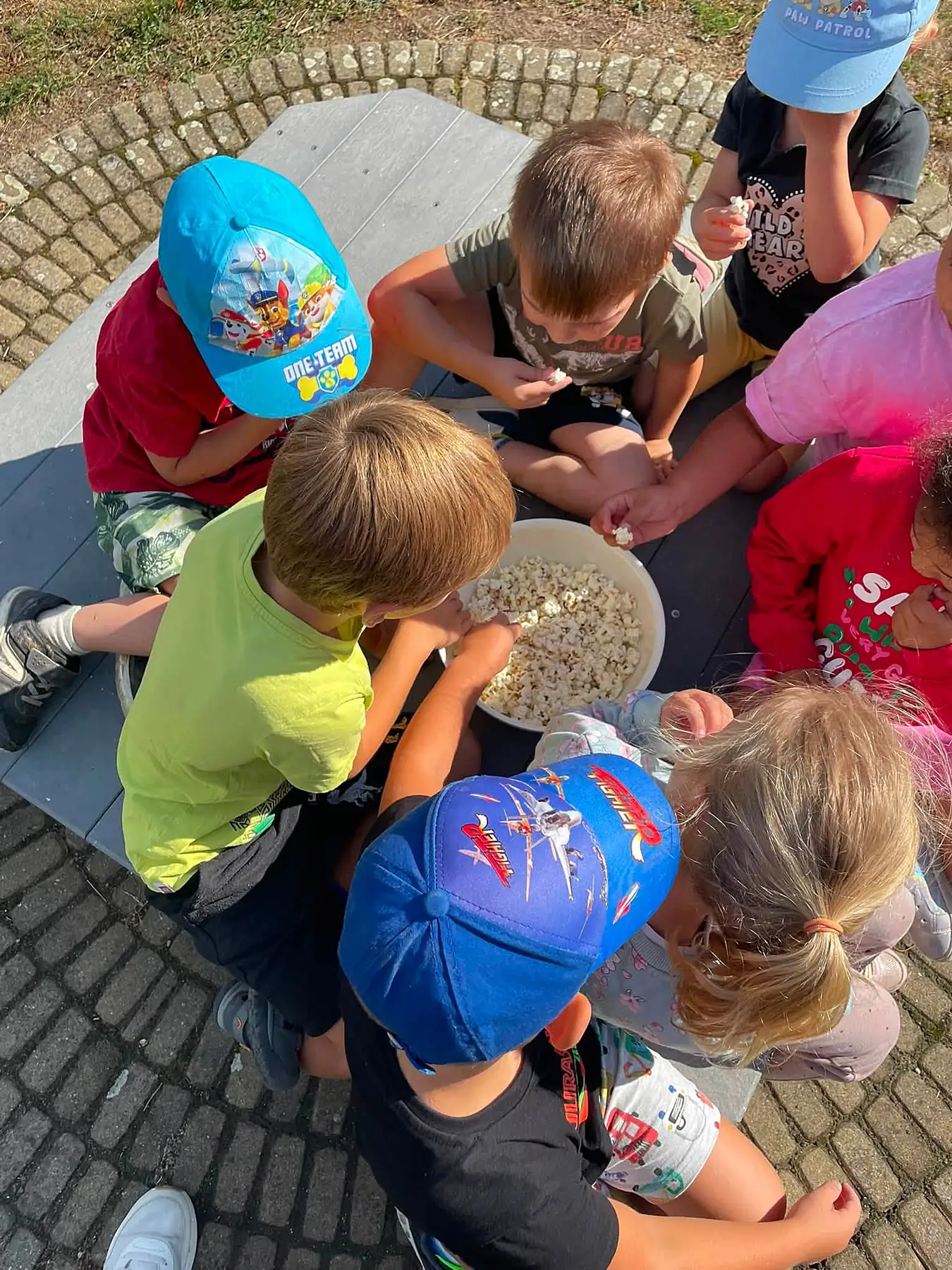 Děti společně u stolu na zahradě při svačince